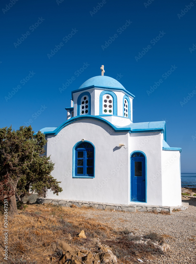 Obraz premium White and blue Greek Orthodox chapel by the sea in Ikaria island under blue summer sky, Greece