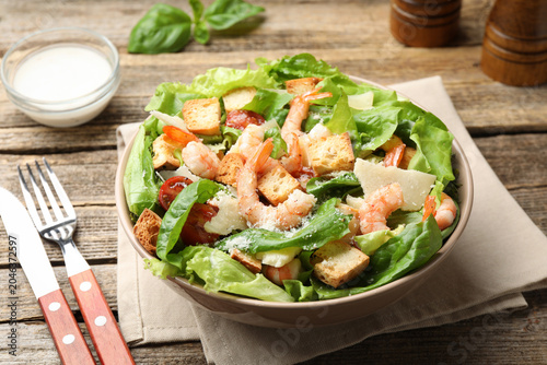 Canvastavla Delicious Caesar salad with shrimps in bowl served on wooden table, closeup