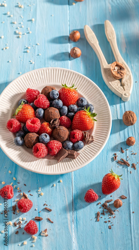 Fresh strawberries, raspberries, blueberries, and chocolate truffles on plate.