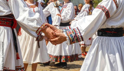 Close-up of people in traditional attire holding hands while dancing outdoors during a cultural festival