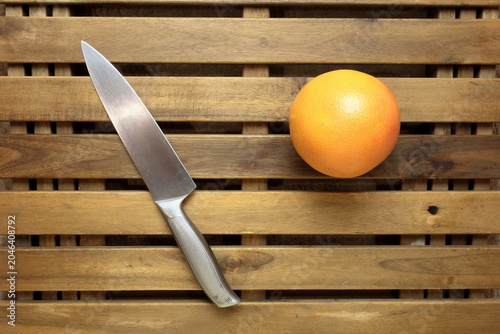 a knife and a grapefruit on a textured wooden table