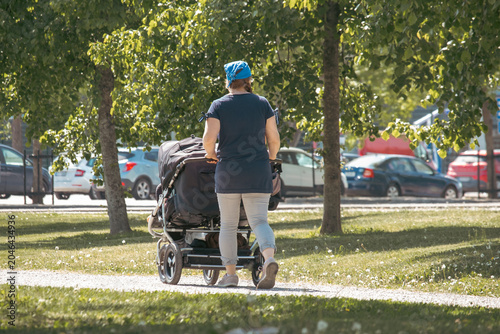Fotografie A young woman walks with a black stroller in a summer park