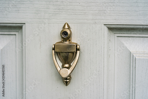 Door knocker on wooden door with a small peephole seen from a close view in daylight