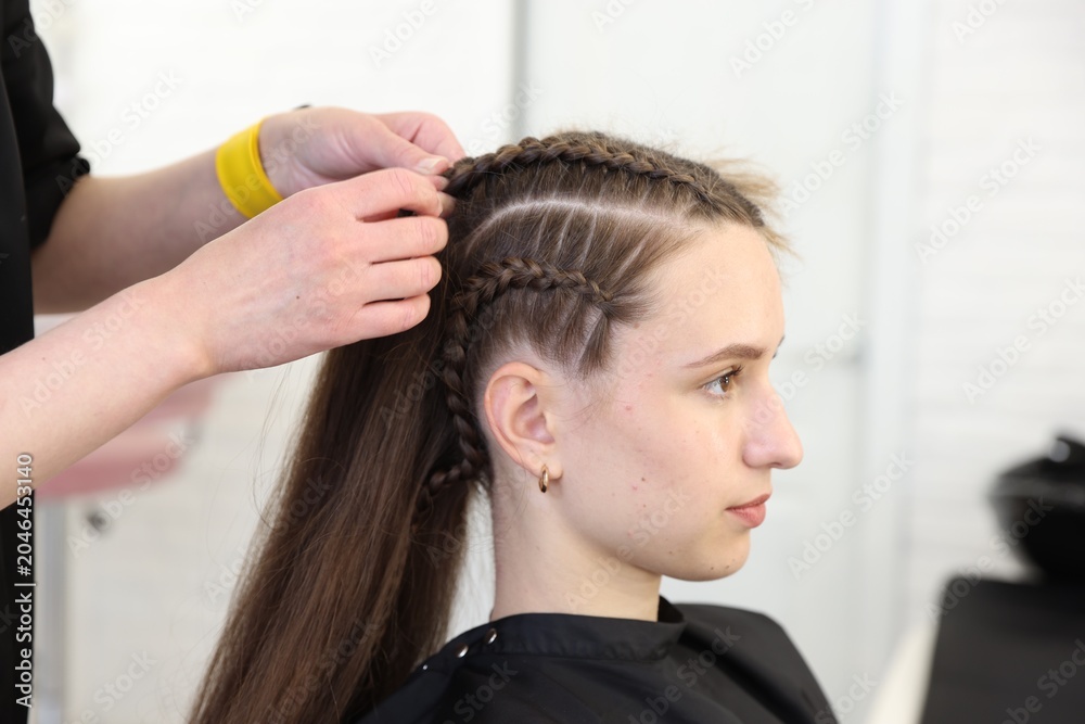 Naklejka premium Hairstylist braiding teenage girl's hair in salon, closeup