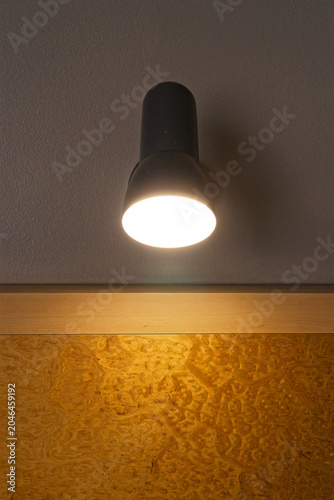 Modern wall-mounted bedside lamp illuminating a decorative wooden element on a gray wall
