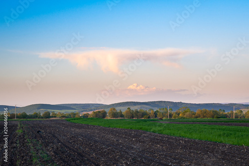 Pink colored cirrus cloud with virga fall streaks over the hilly countryside of central Transylvania, Romania.