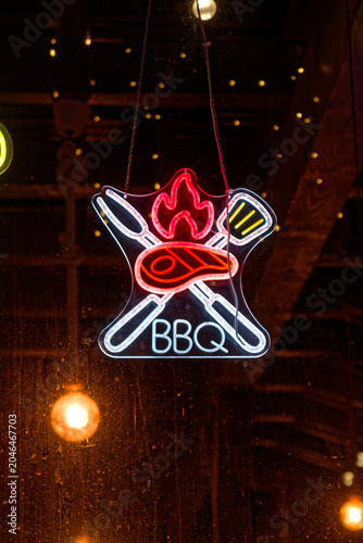 Neon BBQ sign with symbols of fork, spatula, steak, and flame