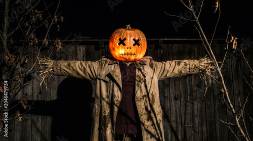 Quadro su tela Scary Halloween scarecrow with a glowing jack o lantern head and straw arms in f