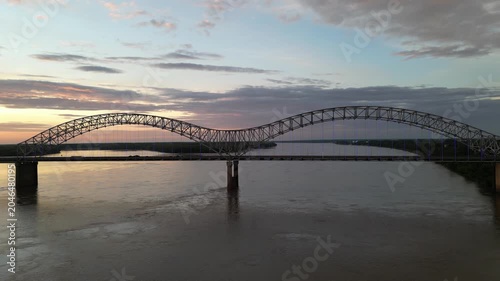 Aerial view of steel arch bridge over wide river at sunset