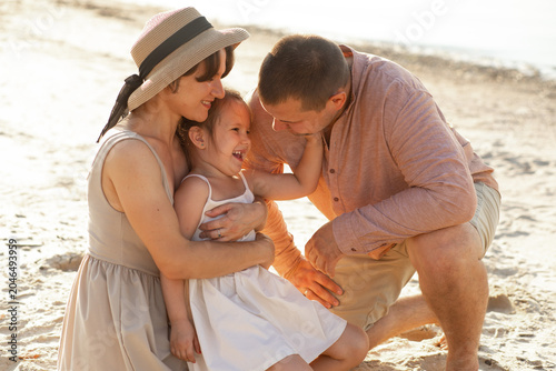 A happy family photo. A family strolls along a sandy beach. A father, mother, and little girl are relaxing on the beach.