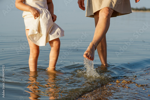 A mother and her little daughter splash in the shallows. Only their feet.