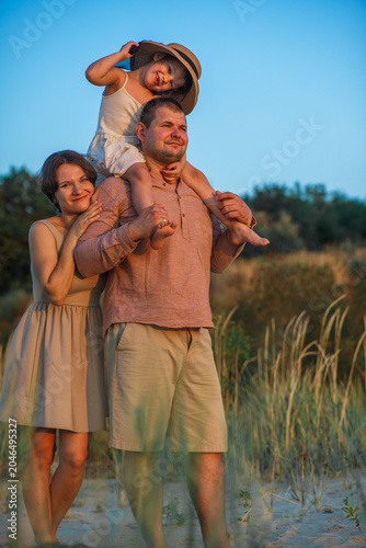 A happy family enjoys the beautiful sunset views. The father put his daughter on his neck.