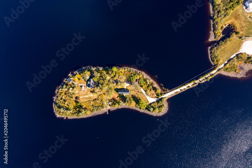 Aerial drone photograph looking directly down on a private island connected by a narrow causeway in Yarmouth Nova Scotia Canada showing waterfront residences surrounded by deep blue lake water