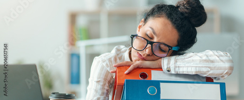 Bild auf Leinwand Worried Asian Woman In Her 30s With Glasses Sleeping At Office Desk With Stack Of Folders, Feeling Fatigued From Work