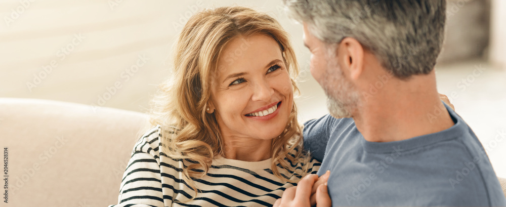 Fototapeta premium Happy Caucasian In Their 40s Smiling While Embracing At Home, Enjoying Time Together On Couch In Cozy Living Room, Displaying Affection And Joy, Family Concept