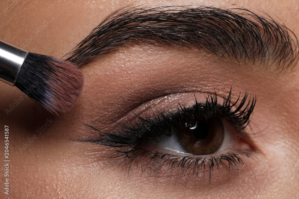 Naklejka premium Applying eye shadow with brush onto woman's face, closeup