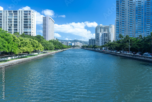 Fotografie Ala Wai Canal cutting through Honolulu’s urban core, flanked by high-rise buildi