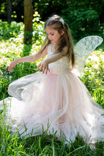 Playful 4 years old girl in a fairy dress dancing and spinning around on the green grass on a sunny day