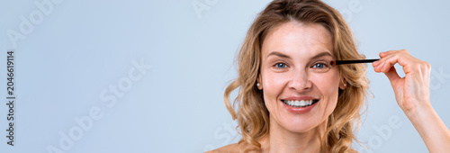 Fotografía Smiling Caucasian Woman In Her 30s Applying Mascara With Makeup Brush In Front O