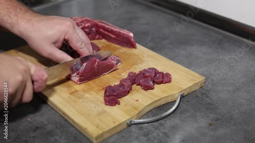 Horizontal 4K video. Male hand cutting piece of raw fresh juicy beef meat with knife on wooden cutting board on kitchen table close up. Concept of healthy food, preparing dinner, lunch, no vegan cafe