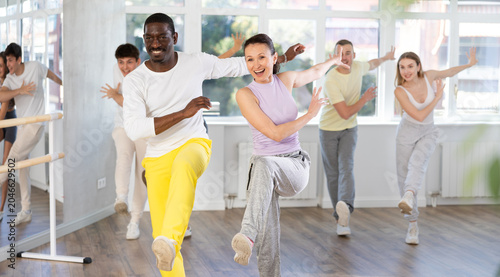 Fotografie Cheerful African American male amateur dancer wearing vibrant yellow sweatpants practicing vigorous playful swing in pair with enthusiastic sporty woman during dance class