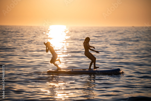 Tableau sur toile Children paddleboarding on water at sunset playing