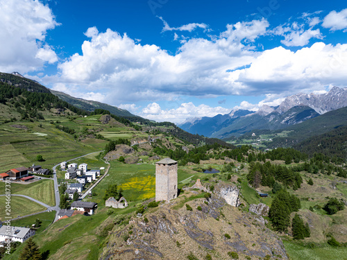 Aerial view of Chaste Steinsberg tower on a rocky hill overlooking the village of Scuol and the alpine mountains under a cloudy sky in Scuol, Graubunden, Switzerland.