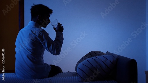 Foto Man sitting up in bed at night, blue light on his face, drinking a glass of wate