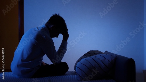 Photos Man sitting on bed in dark bedroom late at night, silhouetted by blue light, res