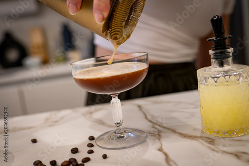 Schilderij op canvas Bartender straining espresso martini into a glass on marble countertop with coff