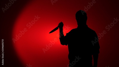 Fotografie Man's silhouette appearing against a red lit background, holding a knife, creati
