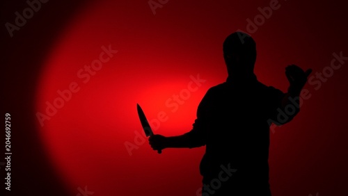 Fotografie Silhouette of a threatening man holding a large kitchen knife against a red back