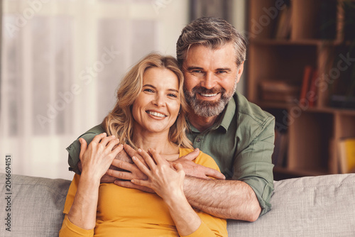 Obraz na płótnie Joyful Caucasian Smiling While Embracing Together At Home, Sitting Comfortably On Couch