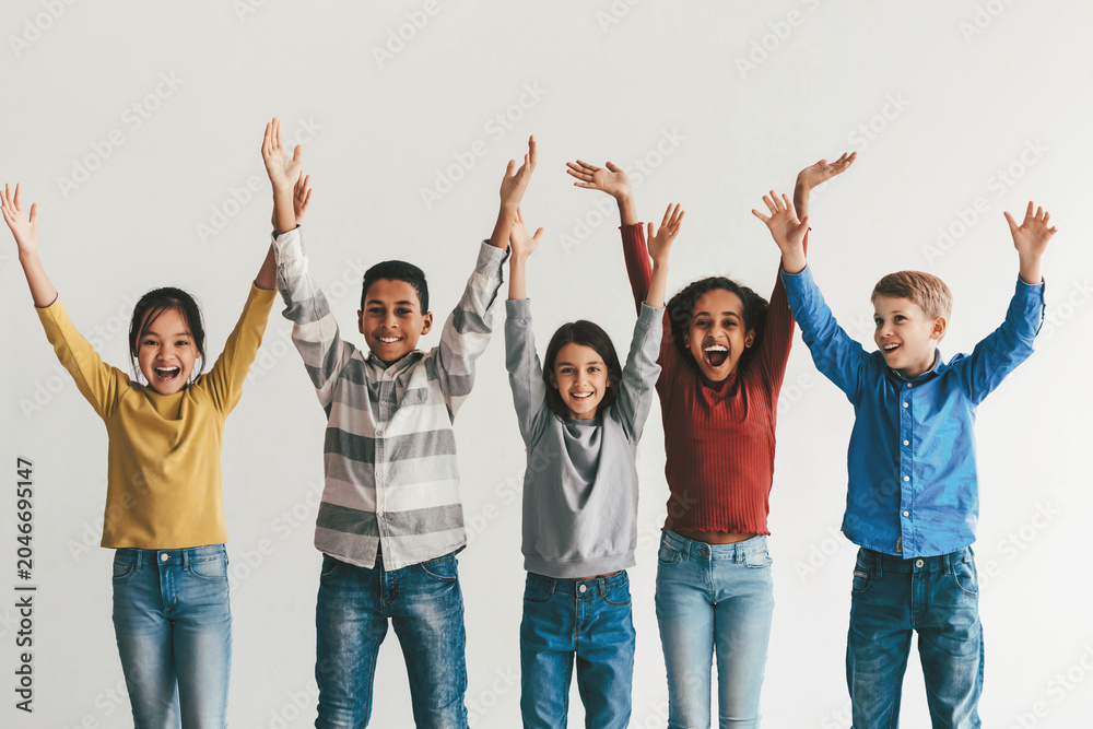 Obraz premium Joyful Diverse Children Including Boys And Girls Of Various Ethnicities, Smiling And Celebrating Together With Hands Raised, Standing In A Bright Studio, Youthful Energy And Togetherness Concept