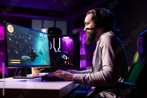 Konstfotografi Man in neon lit apartment having fun with friends playing videogames, talking online using headphones mic, concentrating