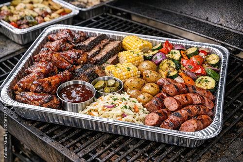 Grilled BBQ spread in aluminium pans with various meats and vegetables