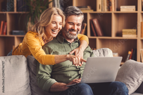 Fotografía Joyful, Man And Woman In Mid-age, Smiling And Engaged While Using Laptop Together In Comfortable Living Room, Sharing Fun Moments