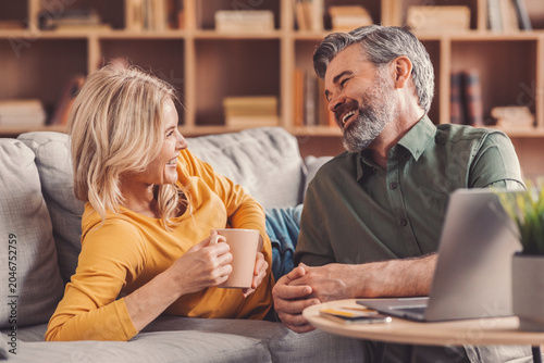 Fotografie Smiling Caucasian Man And Woman Enjoying Each Other's Company And Laughter While Relaxing On A Couch In Cozy Living Room