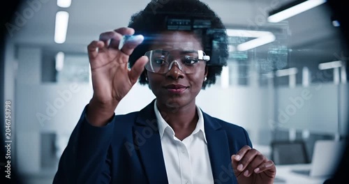 African American woman using augmented reality smart glasses in futuristic corporate office environment
