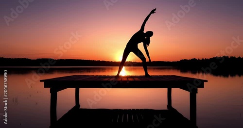 Silhouette of woman practicing yoga at sunset on beach pier, peaceful wellness lifestyle
