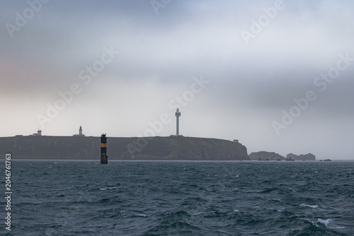 View of the Phare du Stiff lighthouse and radar tower standing on the rugged cliffs of the island under an overcast sky Ushant, Brittany, France.