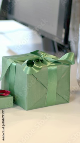 Vertical video: Shifting and zooming camera framing green gift box on desk, centering bow for focus