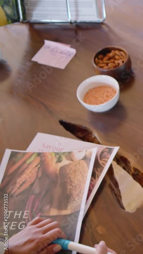 Vertical video: Placing hand with pen on magazines, stirring dip in bowl at table, copy space