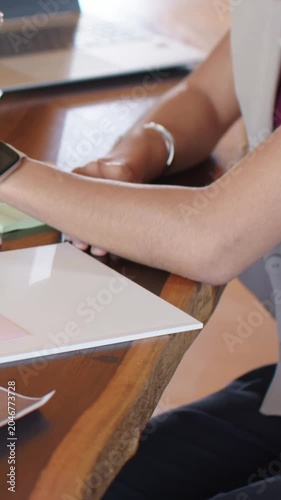 Vertical video: Reaching woman in sleeveless top pausing then grabbing pen at home desk, to write