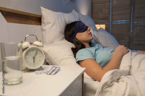 Young woman with mask sleeping after taking melatonin pills in bedroom at night