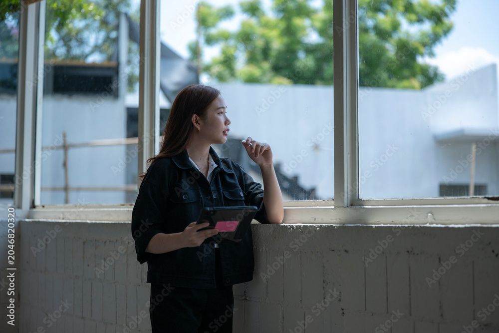 Fototapeta premium Thoughtful woman with tablet gazing out a window in modern space