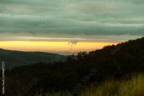 Smoke plume rising from industrial factory over forested hills environmental impact