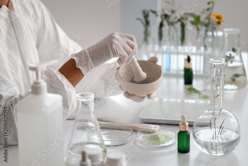 Young African-American female biologist with mortar and pestle working in lab...