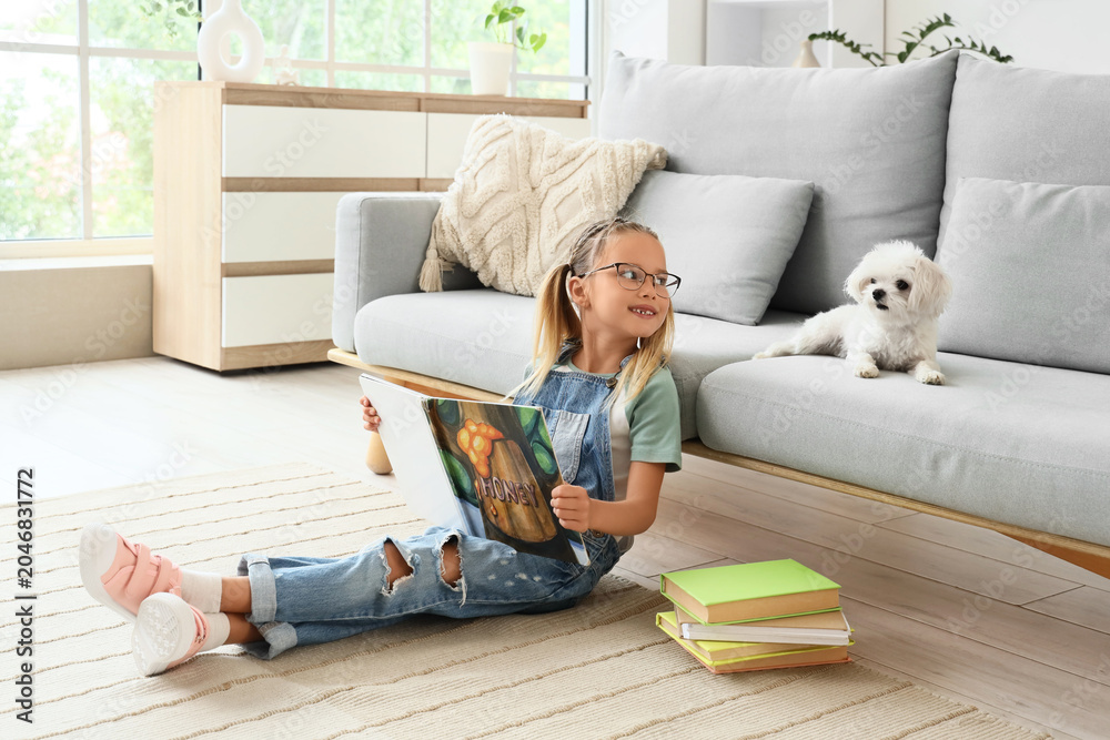 Naklejka premium Cute little happy girl with Maltese dog and books reading on floor at home