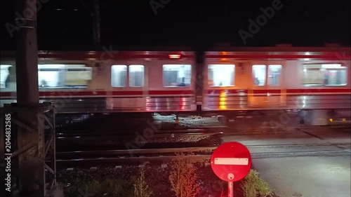 Red commuter train moving fast on tracks at night with blurry window lights
